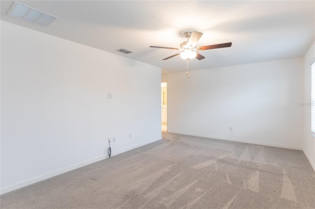 unfurnished room with a ceiling fan, visible vents, light carpet, and baseboards