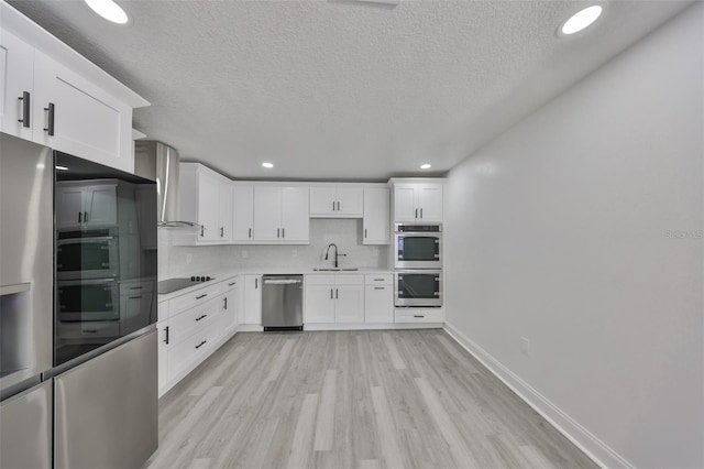 kitchen featuring sink, white cabinetry, appliances with stainless steel finishes, decorative backsplash, and wall chimney range hood