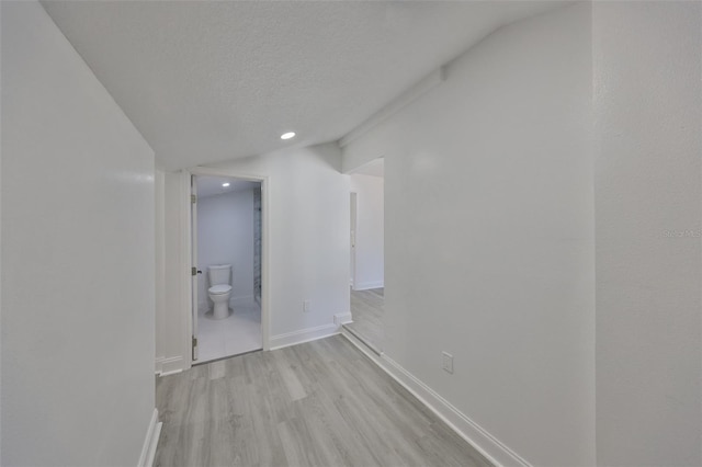 hallway featuring lofted ceiling, a textured ceiling, and light hardwood / wood-style floors