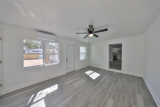 empty room featuring ceiling fan, a wall mounted AC, and light wood-type flooring