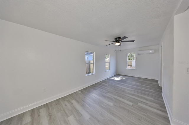 spare room with ceiling fan, a textured ceiling, a wall unit AC, and light wood-type flooring