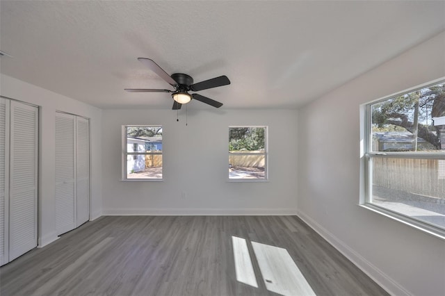 unfurnished bedroom with multiple windows, two closets, wood-type flooring, and ceiling fan