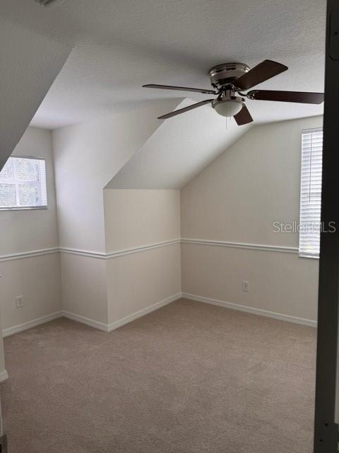 additional living space featuring a textured ceiling, light carpet, vaulted ceiling, and ceiling fan