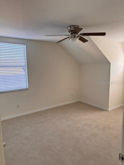 empty room featuring vaulted ceiling, light colored carpet, and ceiling fan