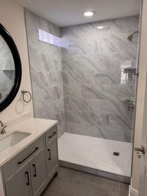 bathroom with tile patterned floors, a tile shower, and vanity