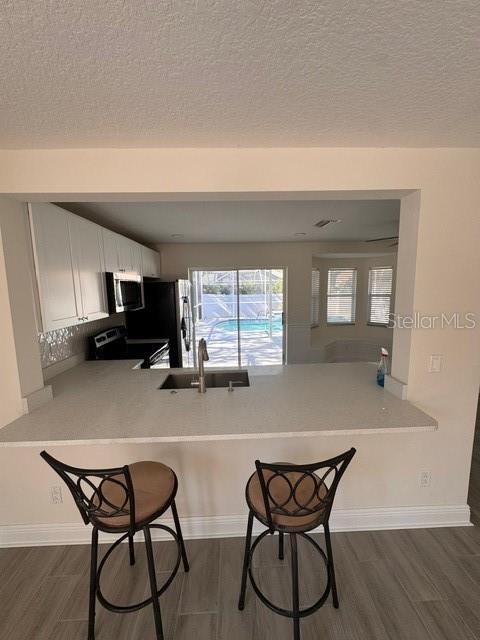 kitchen featuring dark wood-type flooring, stainless steel appliances, white cabinetry, and kitchen peninsula