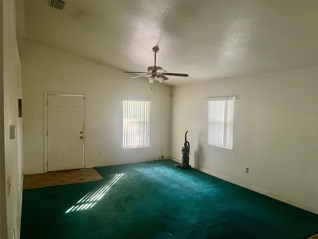 unfurnished room with dark carpet, vaulted ceiling, a textured ceiling, and a wealth of natural light