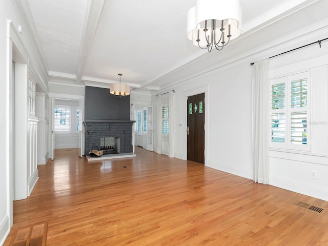 unfurnished living room featuring wood-type flooring, beam ceiling, a fireplace, and a chandelier