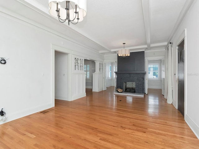 unfurnished living room featuring an inviting chandelier, a brick fireplace, wood-type flooring, and beamed ceiling