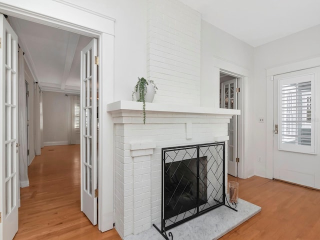 living room featuring a brick fireplace, beam ceiling, and light hardwood / wood-style flooring