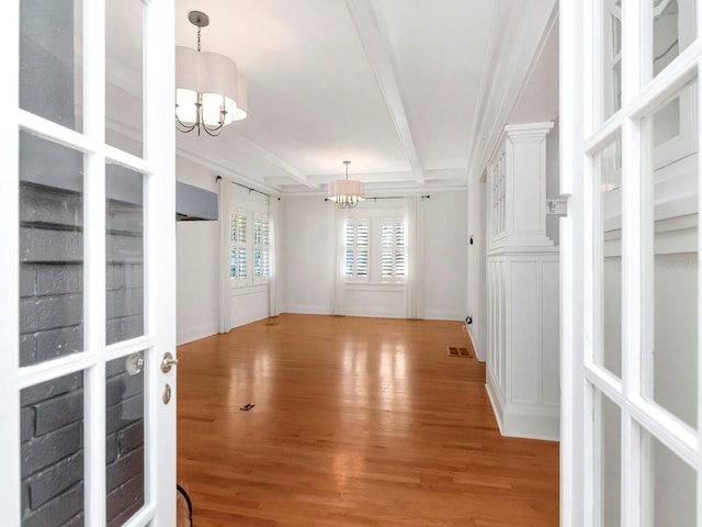 spare room with an inviting chandelier, ornamental molding, and light wood-type flooring