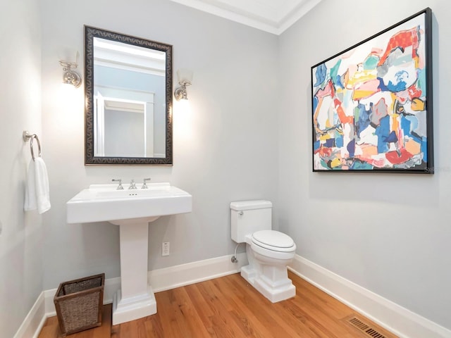 bathroom featuring wood-type flooring, ornamental molding, and toilet