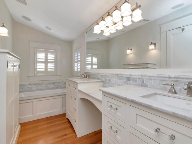 bathroom with vanity, wood-type flooring, decorative backsplash, vaulted ceiling, and a bathing tub