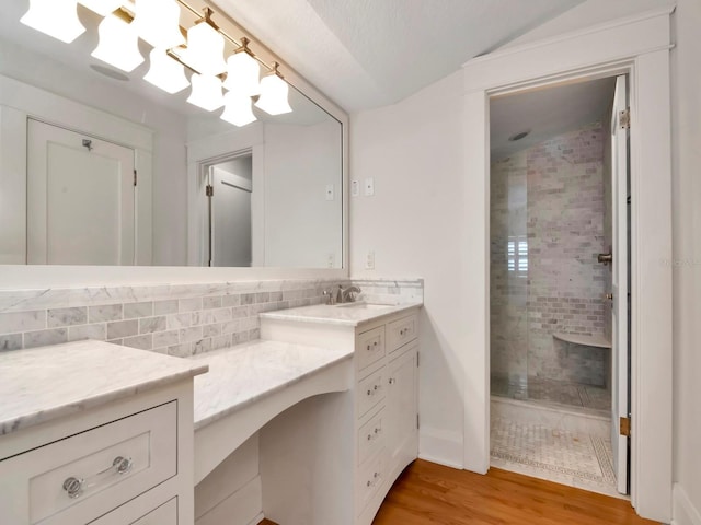 bathroom with a tile shower, backsplash, hardwood / wood-style flooring, vanity, and a notable chandelier