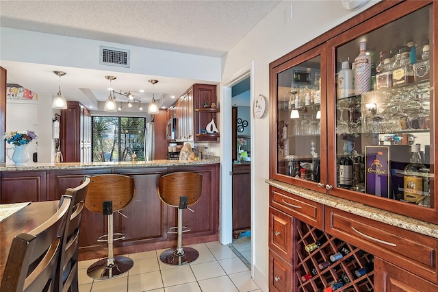 bar with pendant lighting, appliances with stainless steel finishes, light tile patterned flooring, and light stone counters