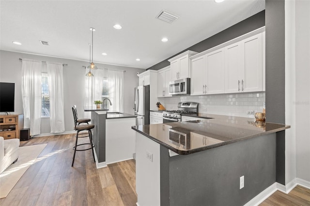 kitchen with appliances with stainless steel finishes, white cabinetry, a center island, a kitchen bar, and kitchen peninsula