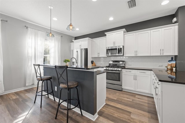 kitchen featuring pendant lighting, stainless steel appliances, an island with sink, and white cabinets