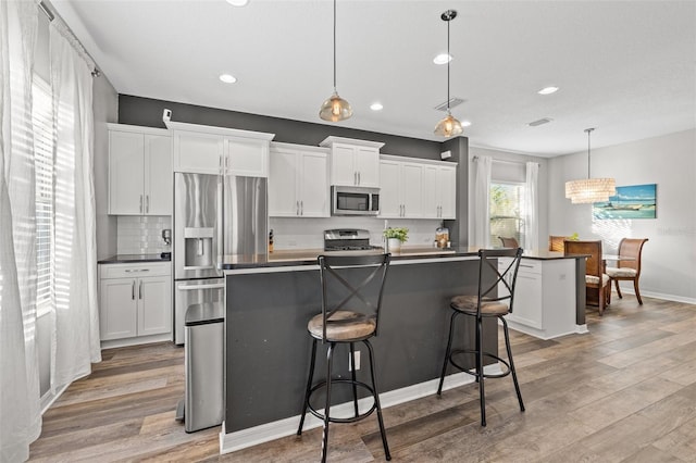 kitchen featuring pendant lighting, stainless steel appliances, an island with sink, and white cabinets