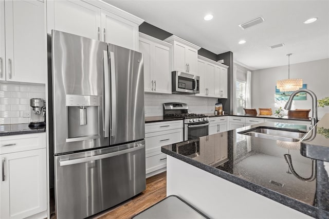 kitchen featuring sink, white cabinetry, stainless steel appliances, decorative light fixtures, and dark stone counters