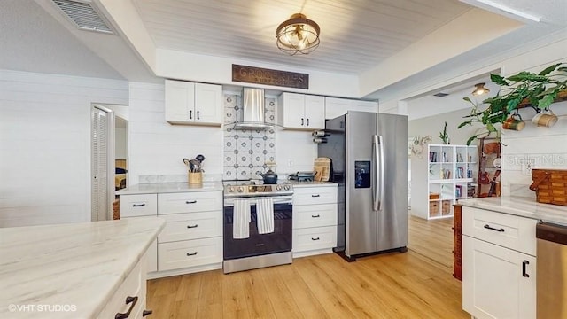 kitchen featuring wall chimney range hood, stainless steel appliances, light stone counters, white cabinets, and light wood-type flooring