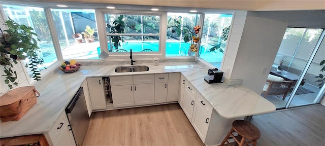 kitchen with sink, white cabinetry, light stone counters, stainless steel dishwasher, and a healthy amount of sunlight