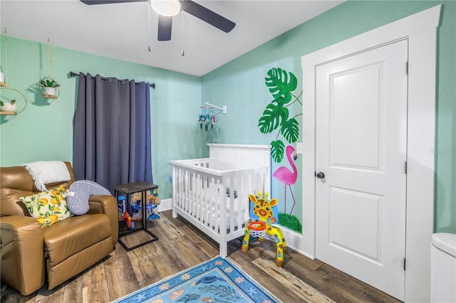 bedroom with a crib, dark hardwood / wood-style floors, and ceiling fan