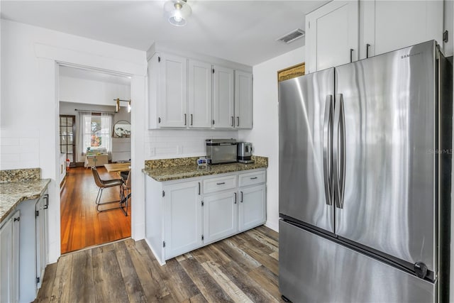 kitchen featuring stainless steel refrigerator, white cabinetry, dark stone countertops, dark hardwood / wood-style floors, and tasteful backsplash