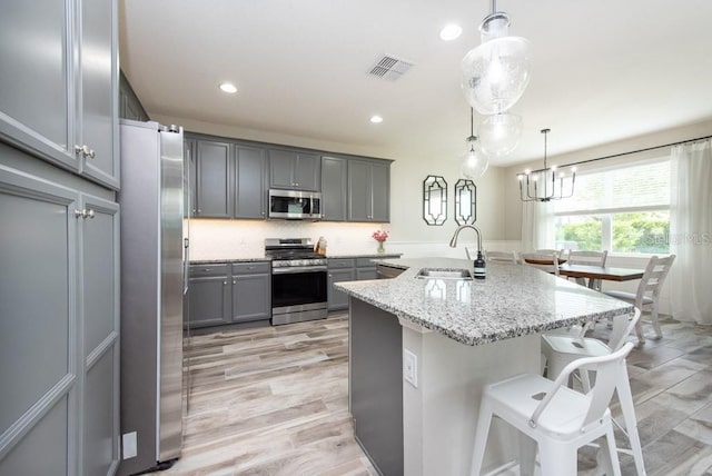 kitchen featuring gray cabinets, light stone countertops, appliances with stainless steel finishes, and decorative light fixtures