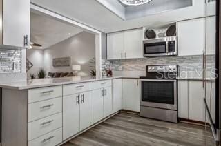 kitchen featuring appliances with stainless steel finishes, backsplash, white cabinets, dark hardwood / wood-style flooring, and a raised ceiling