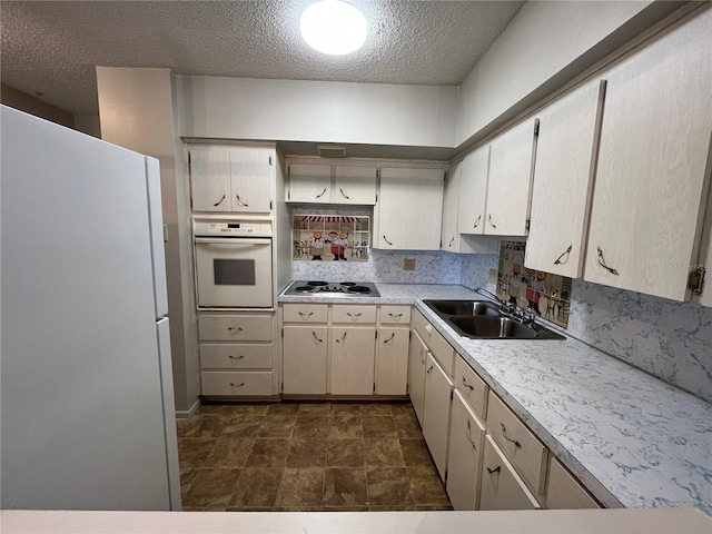 kitchen featuring sink, a textured ceiling, white appliances, and decorative backsplash