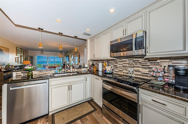 kitchen with sink, dark stone countertops, appliances with stainless steel finishes, kitchen peninsula, and pendant lighting