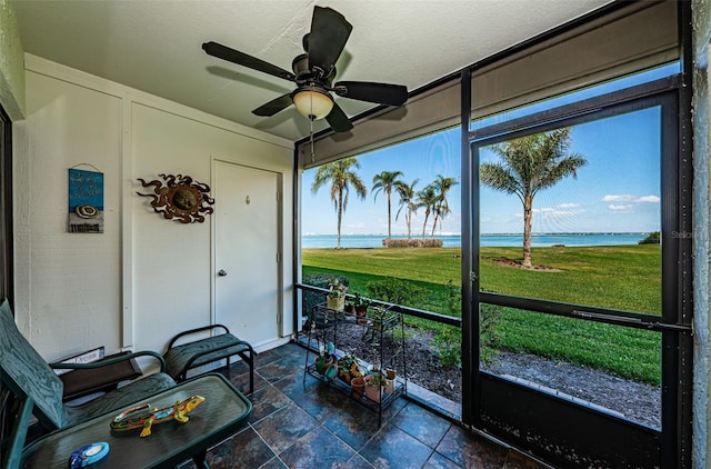 sunroom with ceiling fan and a water view