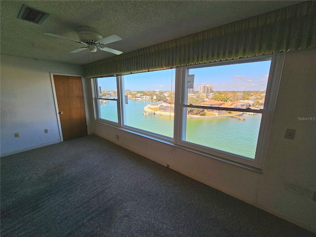 empty room featuring a water view, ceiling fan, carpet flooring, and a textured ceiling