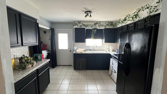 kitchen with sink, black fridge, washer and dryer, light tile patterned floors, and backsplash