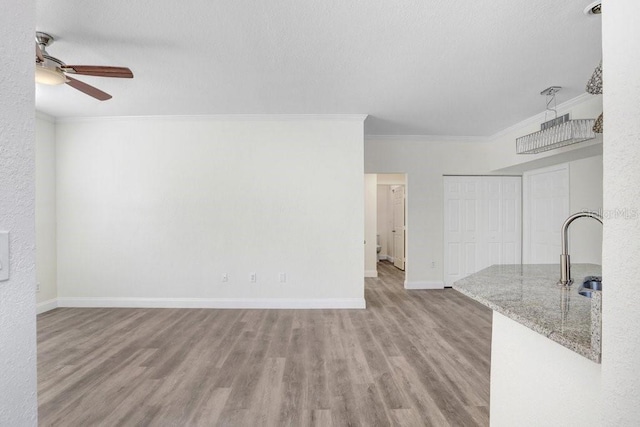 unfurnished living room featuring sink, ornamental molding, ceiling fan, a textured ceiling, and light hardwood / wood-style flooring