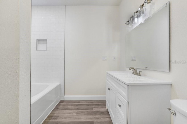 full bathroom featuring wood-type flooring, tiled shower / bath, vanity, and toilet