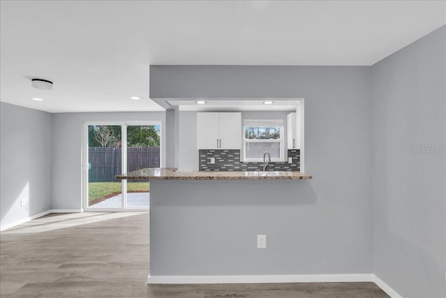 kitchen with white cabinetry, light stone countertops, kitchen peninsula, and tasteful backsplash