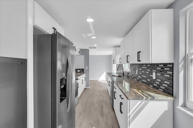 kitchen featuring sink, white cabinetry, stainless steel fridge with ice dispenser, decorative backsplash, and dark stone counters