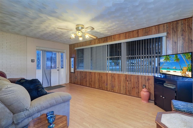 living room featuring a textured ceiling, wood walls, ceiling fan, and light wood-type flooring