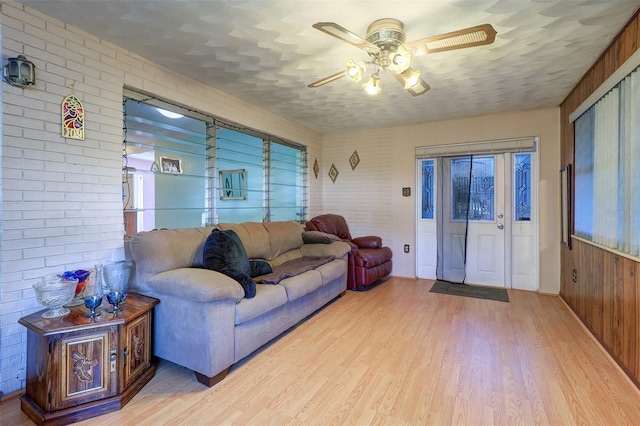 living room featuring ceiling fan, a textured ceiling, brick wall, and light wood-type flooring