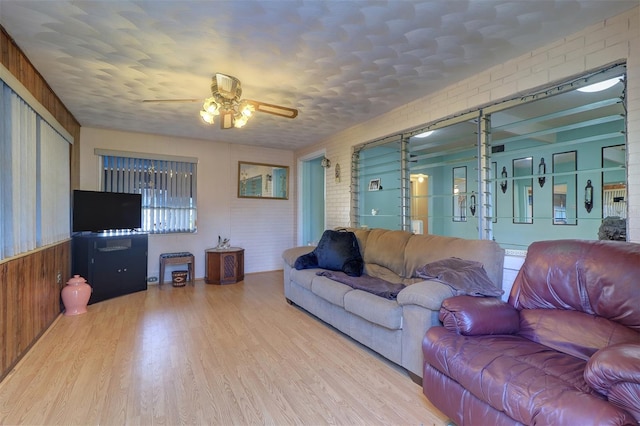 living room with brick wall, wood walls, ceiling fan, and light hardwood / wood-style flooring