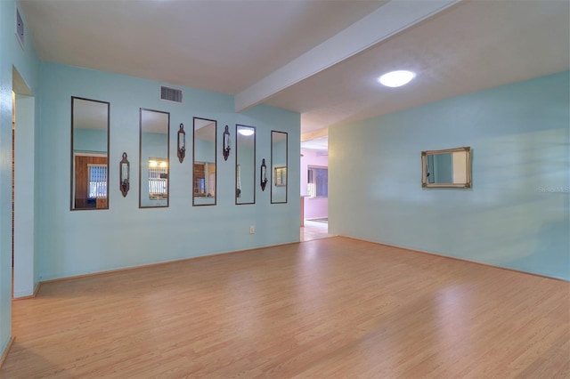 spare room featuring beamed ceiling and light hardwood / wood-style flooring