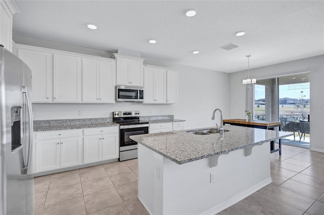 kitchen with sink, hanging light fixtures, an island with sink, stainless steel appliances, and white cabinets