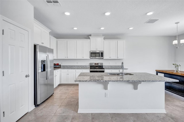 kitchen with an island with sink, sink, white cabinets, light stone counters, and stainless steel appliances