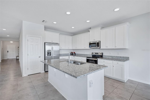 kitchen featuring sink, white cabinetry, stainless steel appliances, light stone counters, and a center island with sink