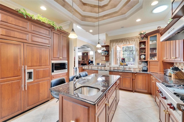 kitchen with built in microwave, decorative light fixtures, sink, and a center island with sink