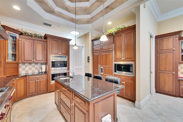 kitchen with pendant lighting, dark stone countertops, light tile patterned floors, stainless steel appliances, and a center island with sink