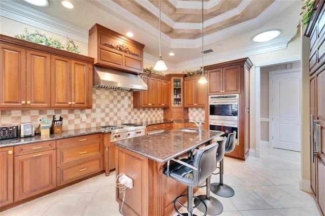 kitchen featuring dark stone countertops, a center island with sink, stainless steel appliances, a kitchen bar, and wall chimney exhaust hood