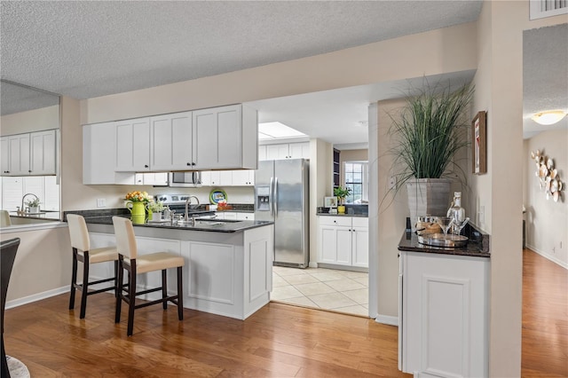 kitchen featuring light hardwood / wood-style flooring, appliances with stainless steel finishes, white cabinets, a kitchen bar, and kitchen peninsula