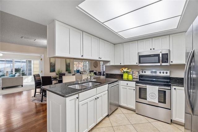 kitchen with white cabinetry, sink, dark stone counters, kitchen peninsula, and stainless steel appliances